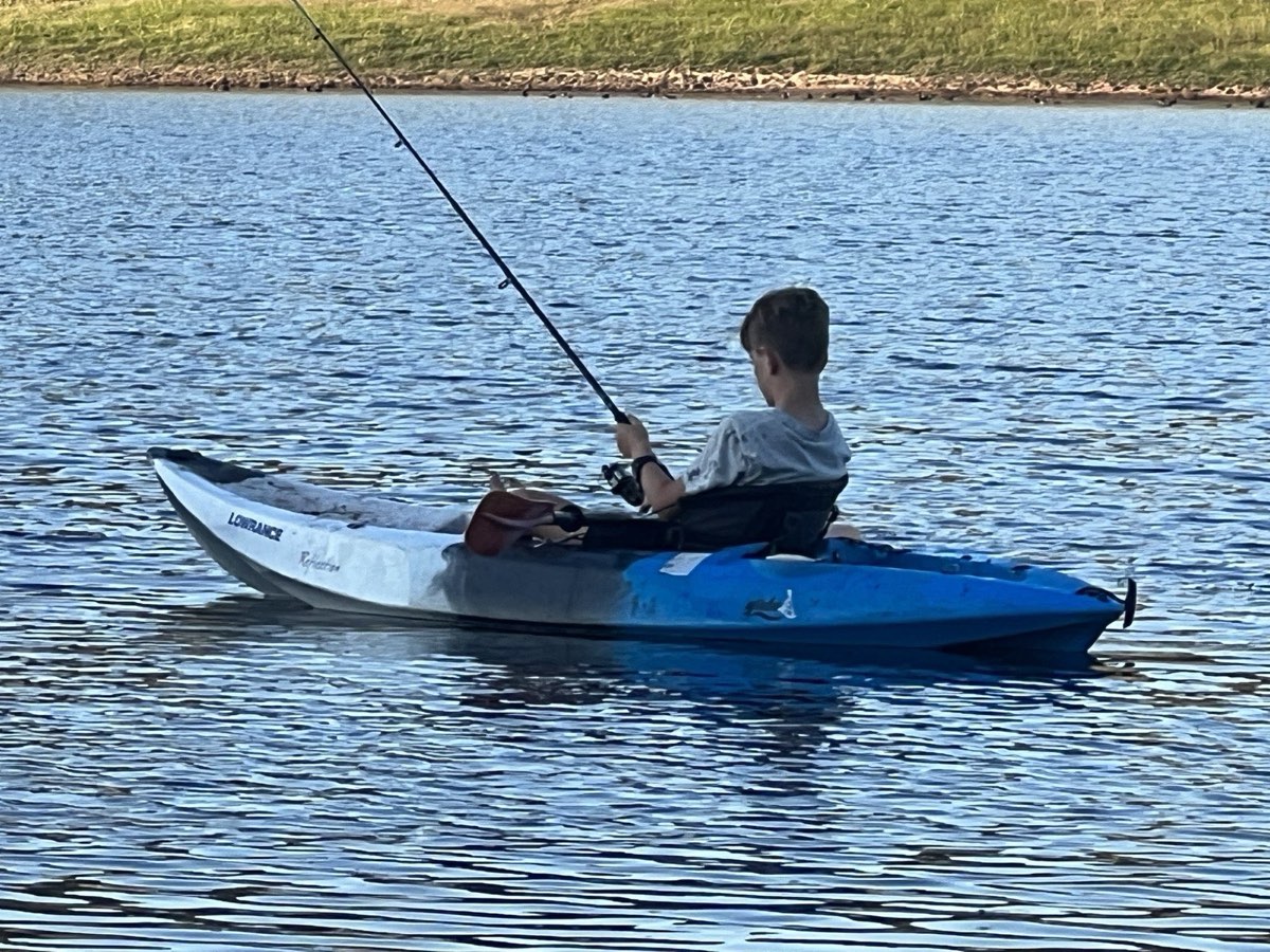 A child fishing from a blue kayak on the lake