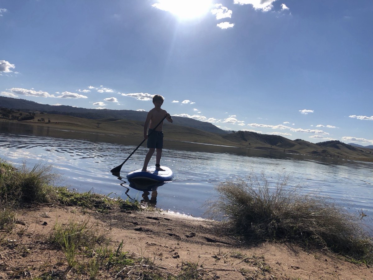 A paddleboarder on the calm lake beside a grassy bank